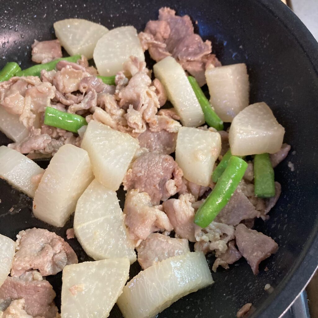 水分を飛ばしている途中の豚肉と大根といんげんが入ったフライパン